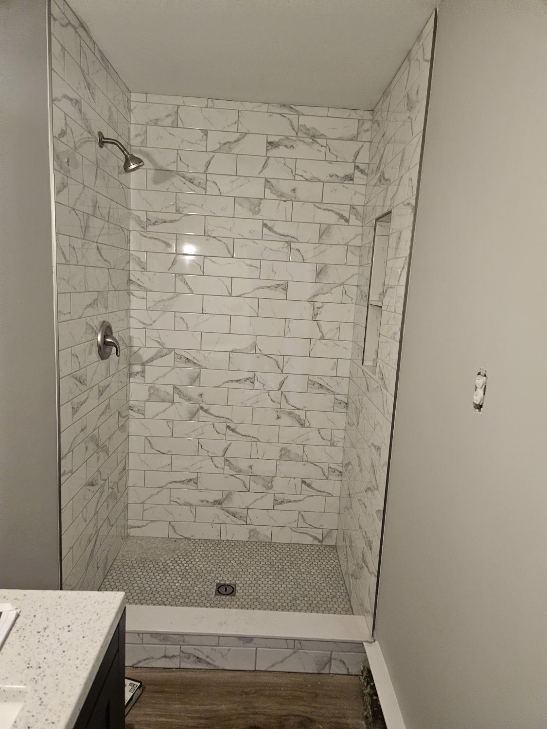 Marble-look subway tile shower with pebble mosaic floor